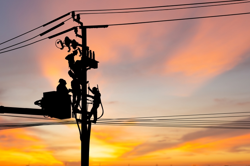 Line workers fix electrical pole during sunset
